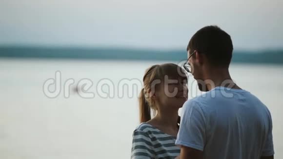 美丽的一对夫妇站在湖边聊天黄昏时分年轻夫妇在海滩上拥抱视频的预览图