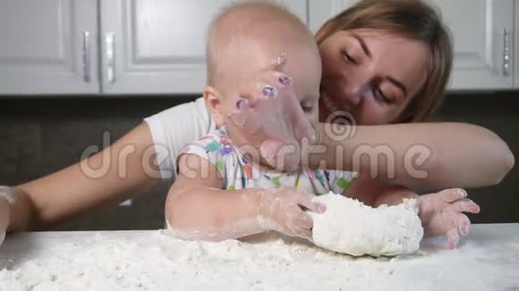年轻的母亲和她的孩子在桌子上准备面团小宝宝玩面粉面包师准备面团视频的预览图
