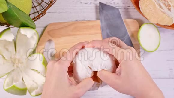 年轻的亚洲妇女正在剥鲜蜜柚在明亮的白色木桌和砧板上的家庭厨房里吃顶部的景色视频的预览图