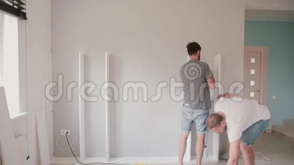 两个年轻人在明亮的客厅里做修理男人一起组装白色家具视频的预览图