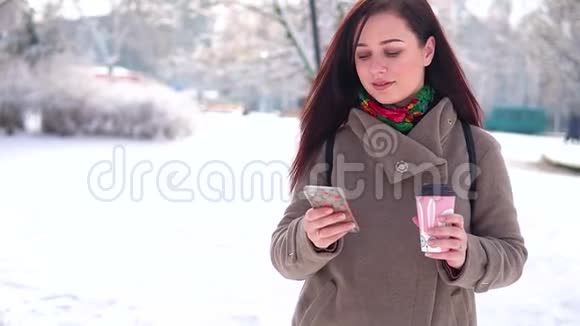 一个年轻的女孩穿着外套漫步在冬季公园写留言喝咖啡视频的预览图