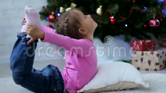 可爱的小女孩在圣诞树旁边的地板上做瑜伽运动视频的预览图