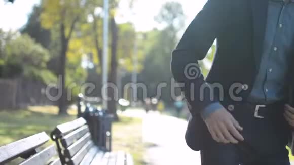 年轻的成功商人穿着西装在阳光明媚的夏日坐在公园的长凳上打电话视频的预览图