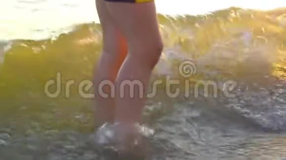 男孩双腿站在海边的水中在海浪中在夕阳的背景下视频的预览图