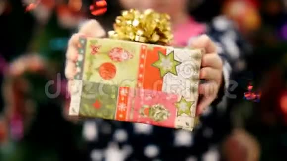 用一个金色的蝴蝶结用一个漂亮的彩色纸包装着一个圣诞礼物两只孩子的手紧紧地握着视频的预览图