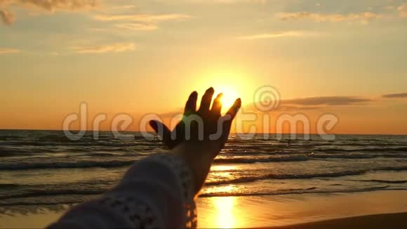 女孩伸出的手是特写的抚摸着阳光在大海慢慢衰落的背景下视频的预览图