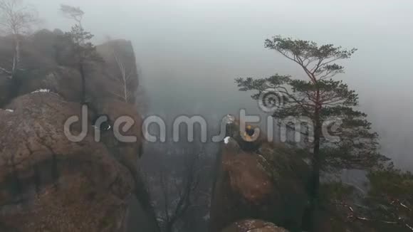 在冬天坐在岩石顶部的人的视野被雾笼罩着视频的预览图