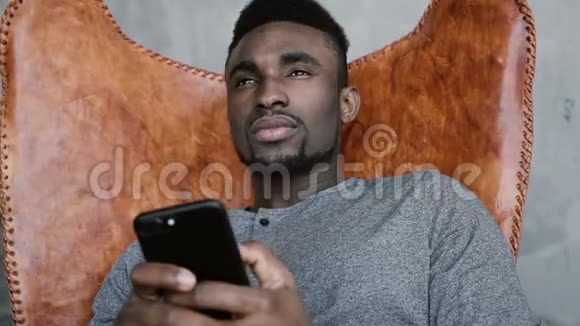 非洲男性坐在椅子上思考拿着智能手机人记得一些美好的东西开始输入信息视频的预览图