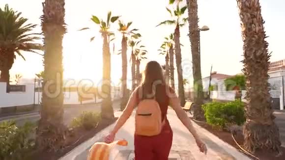 日落时分戴着一顶黄色大帽子的幸福女人在棕榈巷散步视频的预览图