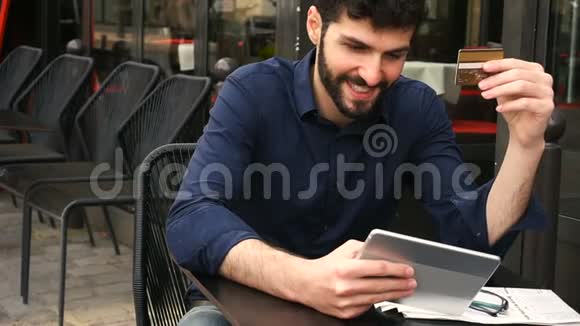 快乐的男人在街边咖啡馆用卡片和平板电脑网上购物表情很慢视频的预览图