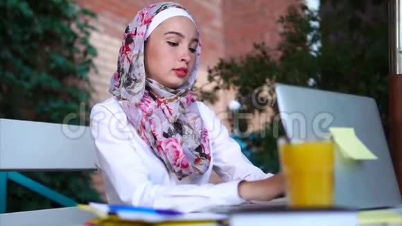 一位现代穆斯林妇女戴着头巾在笔记本电脑上给她的朋友打印信息视频的预览图
