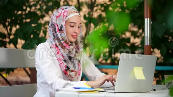 戴头巾的穆斯林学生在夏天的公园里用笔记本电脑写一篇文章视频的预览图