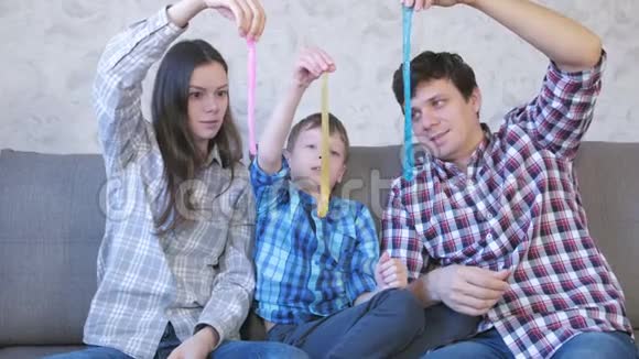 快乐的家庭妈妈儿子和爸爸玩泥浆坐在沙发上把黏液拉出来视频的预览图