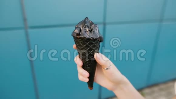 黑色木炭冰淇淋在一只蓝色背景的雌性手中视频的预览图