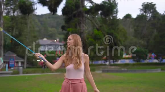 一个年轻女人在公园里做一个大肥皂泡的慢镜头视频的预览图