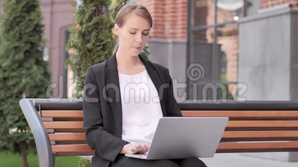 年轻的女商人在笔记本电脑上工作坐在室外的长凳上视频的预览图