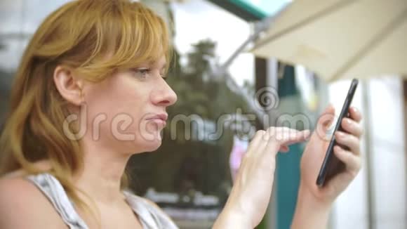 不满意的女孩坐在街上的咖啡馆里看电话视频的预览图