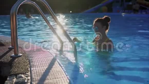 年轻漂亮的女人在游泳池里爬上梯子阳光视频的预览图