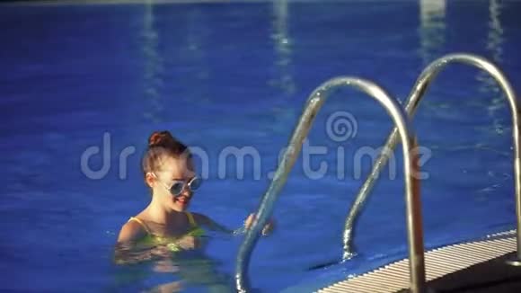 年轻漂亮的女人在游泳池里爬上梯子阳光视频的预览图
