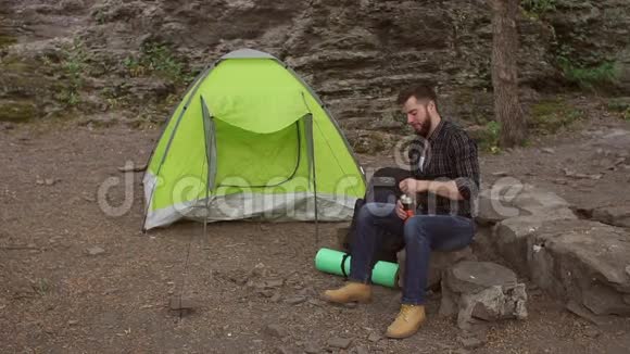 旅行者坐在帐篷旁边喝水视频的预览图