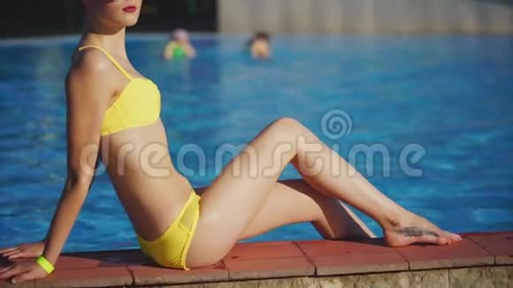 在游泳池附近阳光下晒太阳的身材好的女孩炎热的夏天天气视频的预览图