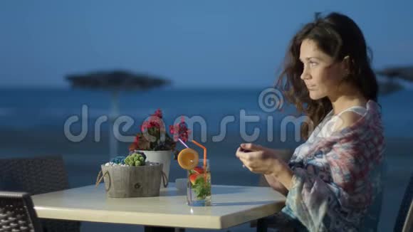 在海滩餐厅享受休息的浪漫女人通过电话发送信息视频的预览图