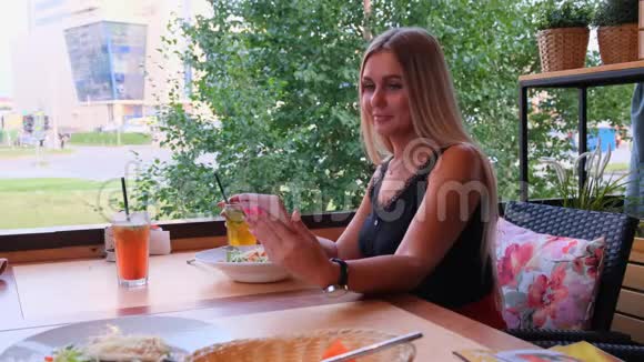 美丽的金发女人在电话里聊天在Skype上聊天喝着鸡尾酒坐在街上的咖啡馆里视频的预览图