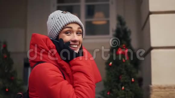 穿着红色夹克的漂亮女孩在一个明亮的冬日站在大街上用智能手机说话视频的预览图