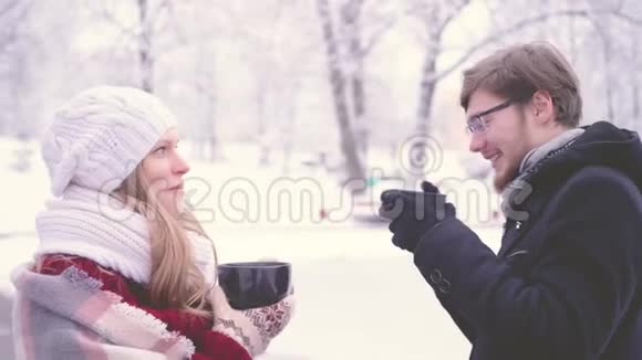 在冬天的公园里美丽的女人和长胡子的男人拿着眼镜一边说一边喝着杯子里的热可可视频的预览图