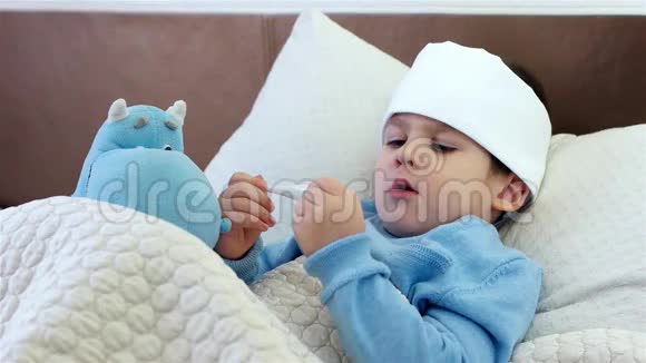 孩子咳嗽男孩脖子上戴着围巾孩子玩电子体温计躺在床上高温视频的预览图