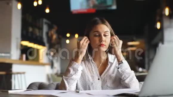 年轻漂亮的女商人在咖啡馆里用耳机听音乐用手提电脑视频的预览图
