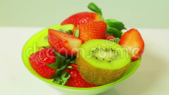 鲜奇异果和切片草莓在蓝色背景上的绿色盘子旋转成一个圆圈从上面看视频的预览图