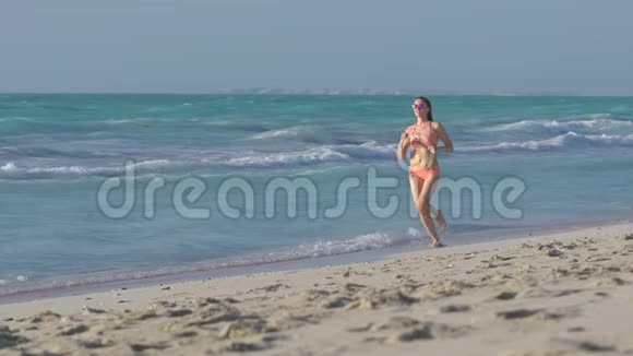 穿着粉红色比基尼的金发女孩在公共海滩上奔跑穿着泳衣的漂亮年轻女子正在跑步和从事视频的预览图