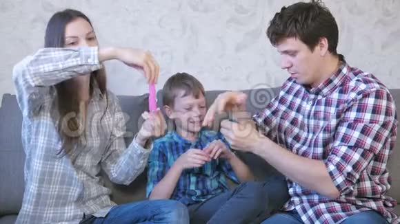 快乐的家庭妈妈儿子和爸爸玩泥浆坐在沙发上把黏液拉出来视频的预览图