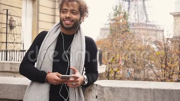 年轻的男性模特在埃菲尔铁塔附近与智能手机聊天听音乐视频的预览图