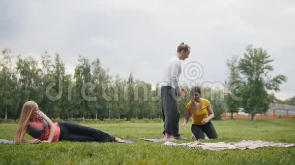 男教练正在训练年轻女性的柔韧性晨间公园的瑜伽练习视频的预览图