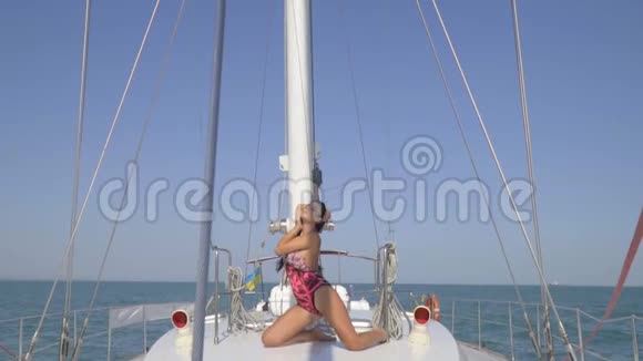 一位身穿泳装的豪华黑发女郎跪在游艇中间挽着她的头发享受着阳光明媚的天气慢慢地视频的预览图