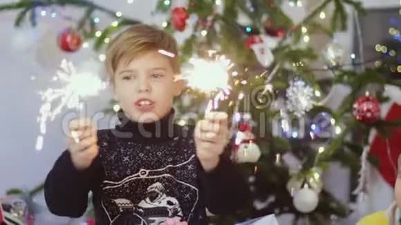 快乐的男孩在圣诞树上的bokeh灯和花环之间燃烧着火花慢动作3840x2160视频的预览图