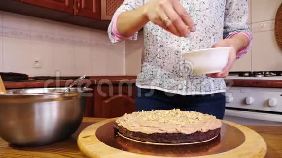 在巧克力海绵蛋糕奶油上浇坚果的女人手的特写视频的预览图