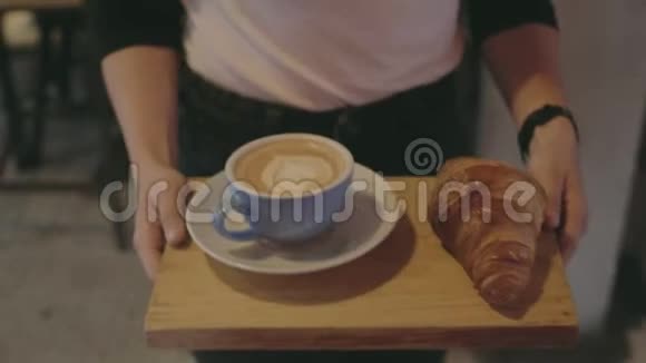 服务员端着咖啡和羊角面包在咖啡馆的餐桌上视频的预览图