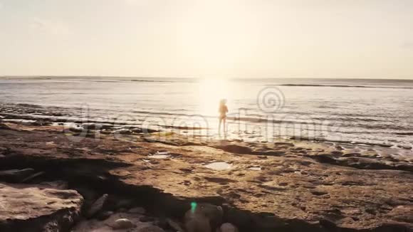 在美丽的日落中站在海滩上观看海景的年轻有思想的女人视频的预览图