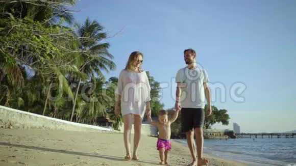 幸福的一家人在海滩上牵着手挥舞着一个小女孩妈妈爸爸女儿在海滩上散步概念视频的预览图