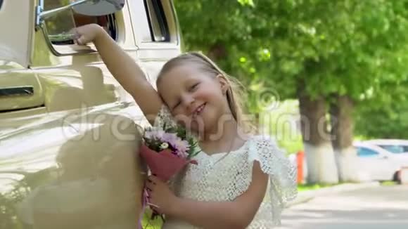 小女孩穿着一件漂亮的浅色连衣裙带着一小束鲜花在米色的复古车上花了很多钱视频的预览图