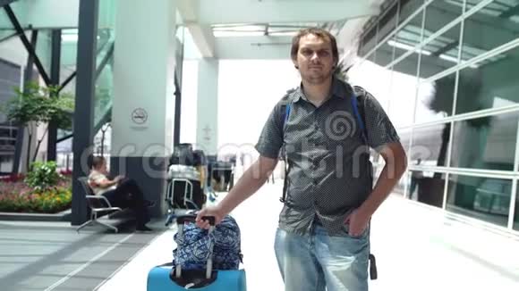 年轻的快乐男子背包拉手提箱在现代机场航站楼旅行的帅哥和他的视频的预览图