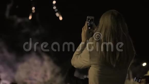 女孩在智能手机上射击敬礼年轻女孩在智能手机上拍摄烟花城市假日视频的预览图