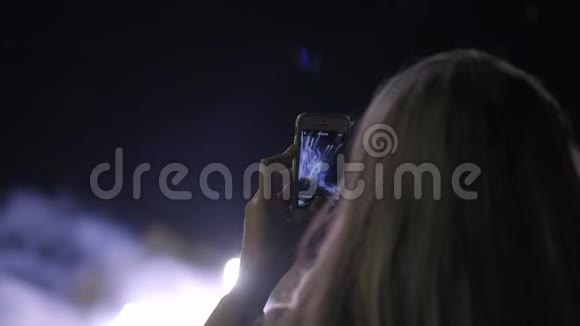 女孩在智能手机上射击敬礼年轻女孩在智能手机上拍摄烟花城市假日视频的预览图