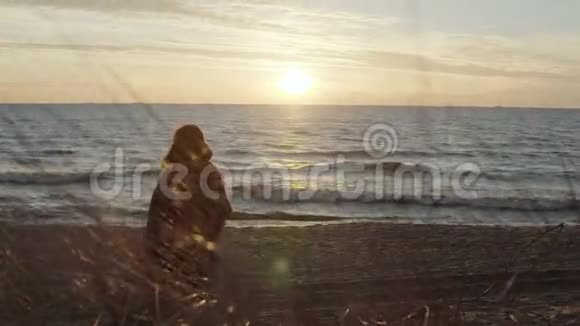 海边有格子花格子的年轻女子的后景眺望远方日落时分在海滩上的一个女人视频的预览图