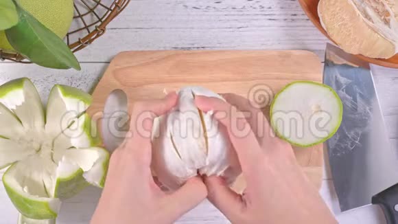 年轻的亚洲妇女正在剥鲜蜜柚在明亮的白色木桌和砧板上的家庭厨房里吃顶部的景色视频的预览图