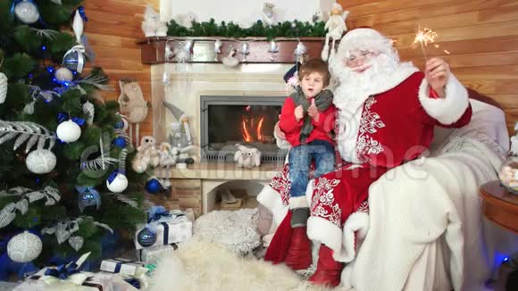 小男孩坐在圣诞老人的腿上闪闪发光节日气氛孩子和快乐的圣诞老人视频的预览图