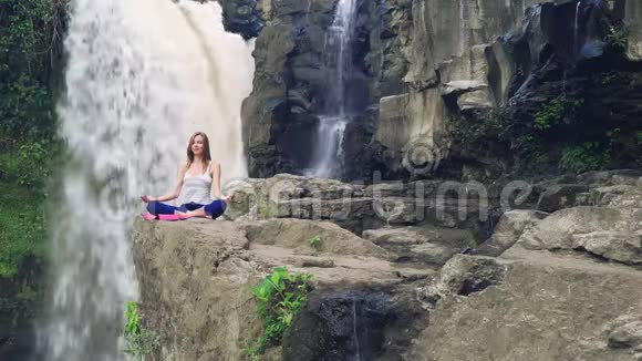 女子坐在瑜伽莲花的姿势旁边的泰根甘瀑布视频的预览图